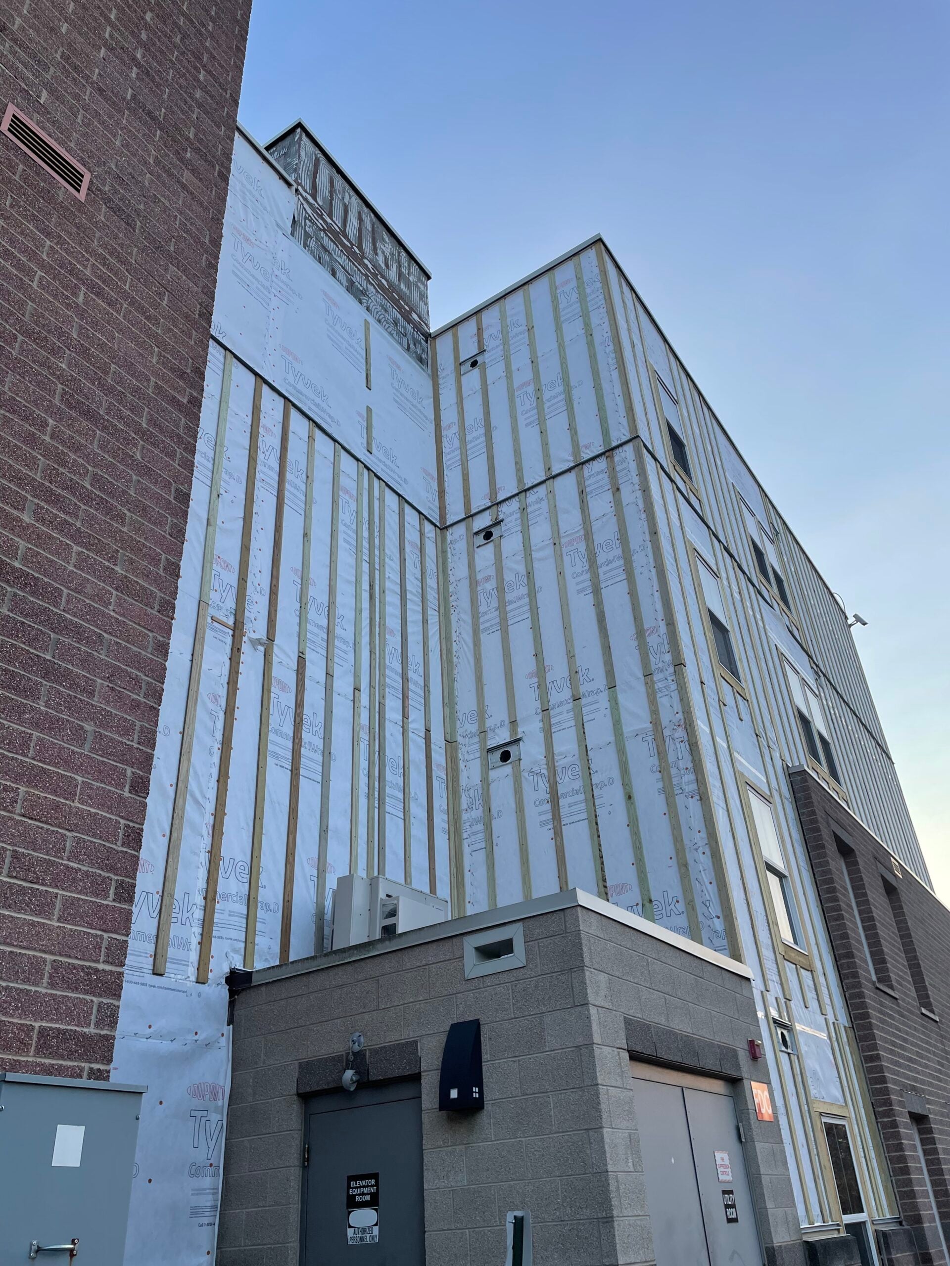 Commercial exterior renovation in progress with weather barrier, furring strips, window openings, and masonry walls prepared for new siding.