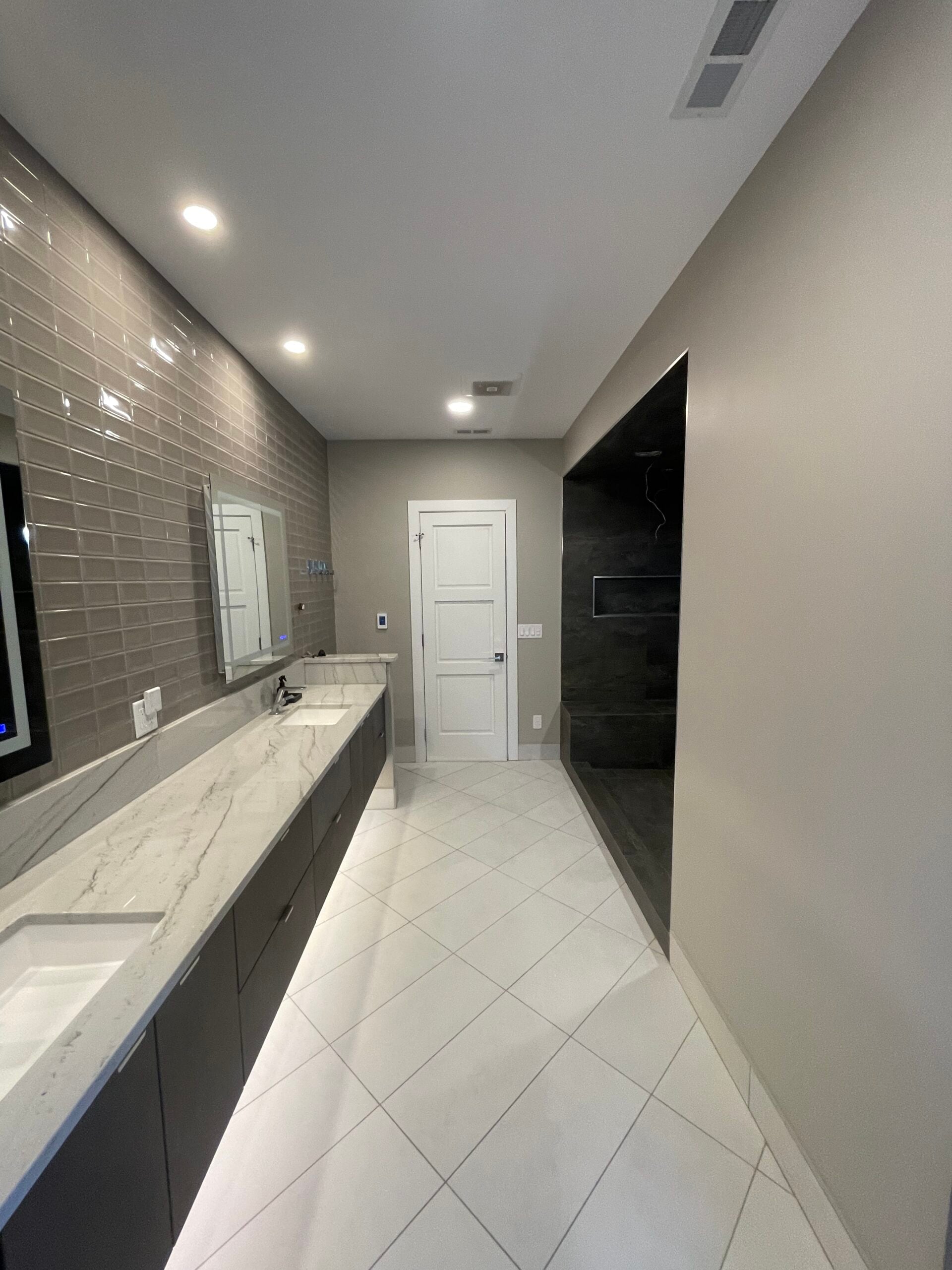Modern bathroom remodel with a long double vanity, marble-look countertop, glossy wall tile, white floor tile, and walk-in shower.