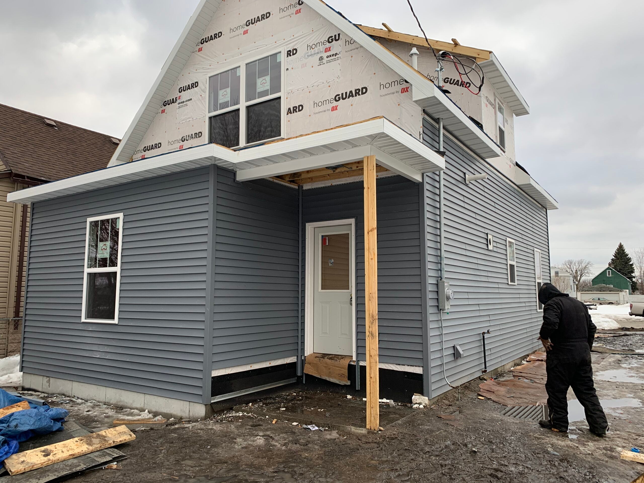 Side and rear view of an exterior remodeling project with new gray siding, replacement windows, and covered entry construction.