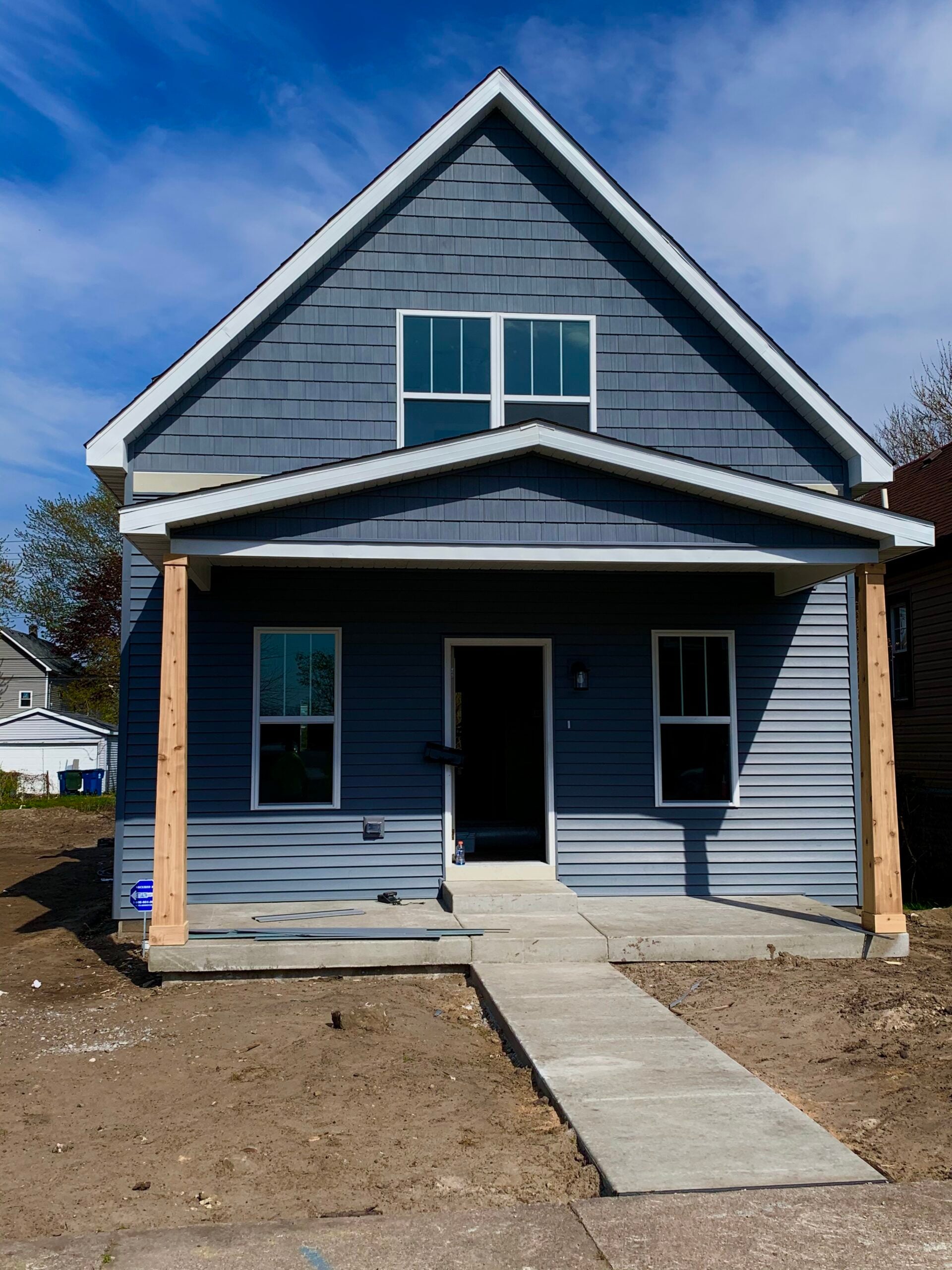 Completed exterior remodel with blue-gray siding, white trim, new windows, and a covered front porch.