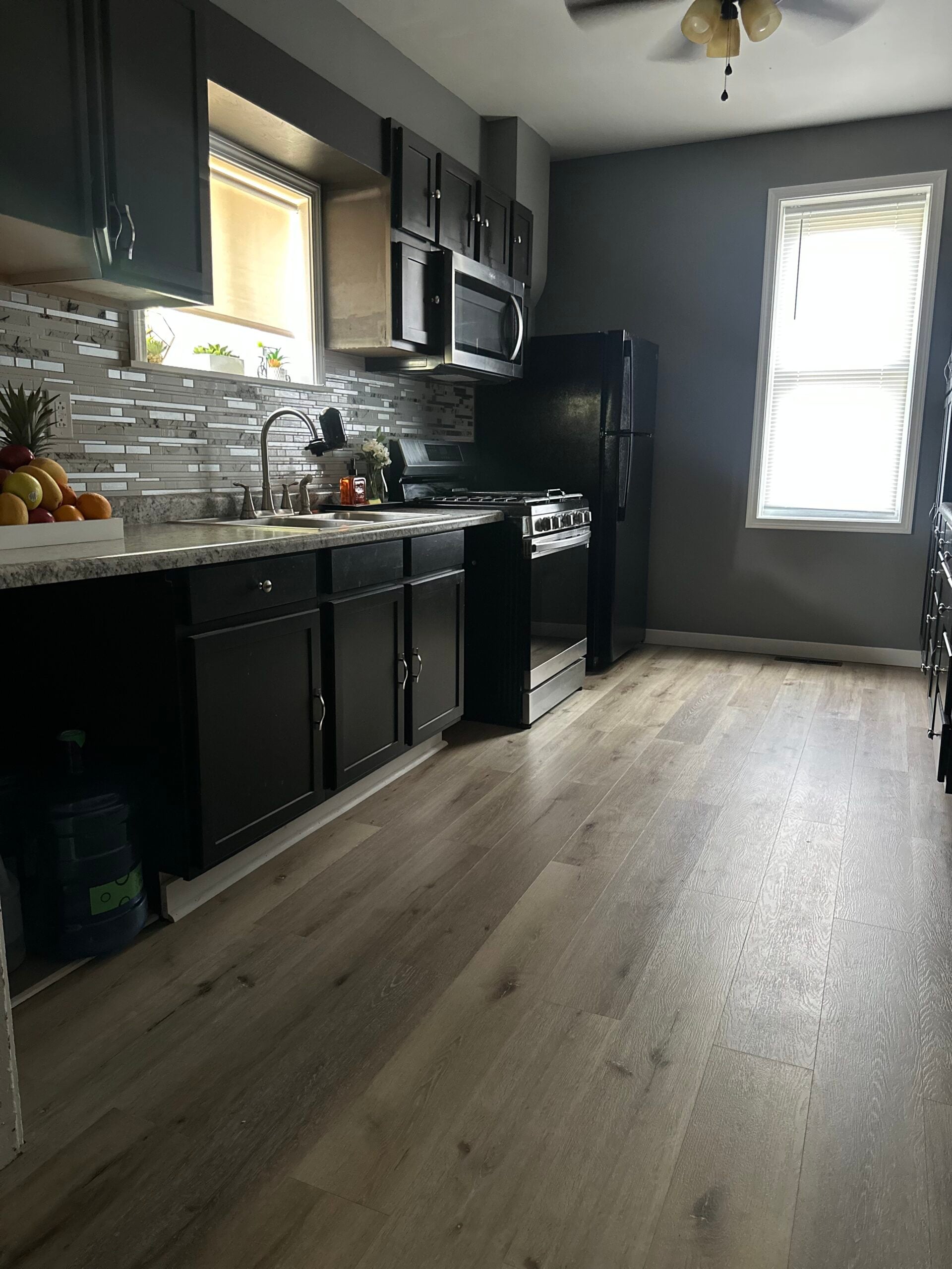 Updated kitchen with dark cabinets, mosaic tile backsplash, stainless steel appliances, and wood-look flooring.