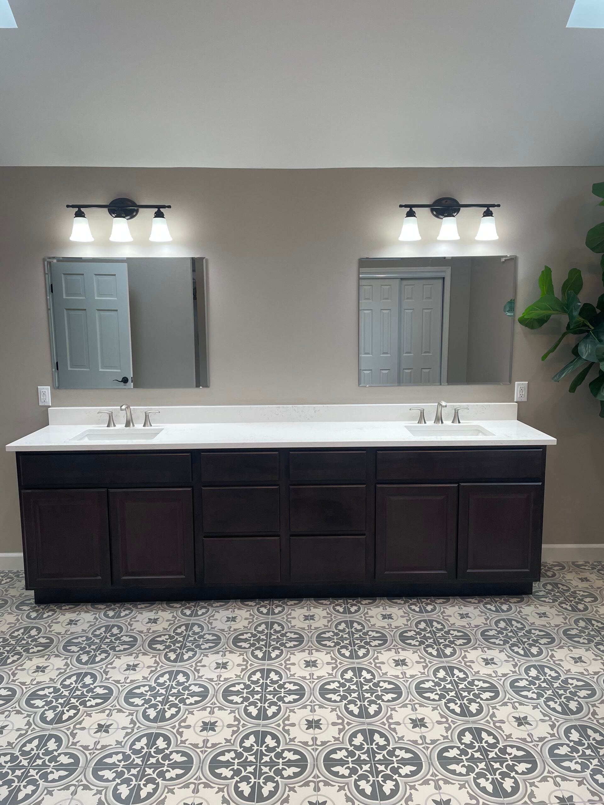 Double vanity bathroom remodel featuring dark wood cabinets, white countertops, modern lighting, and decorative floor tile.