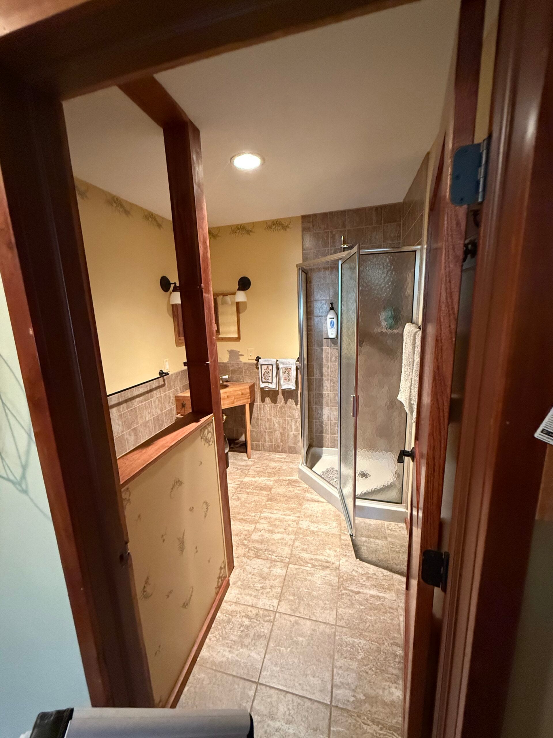 Bathroom before renovation featuring dated tile flooring, yellow walls, wood partitions, and a small enclosed shower.