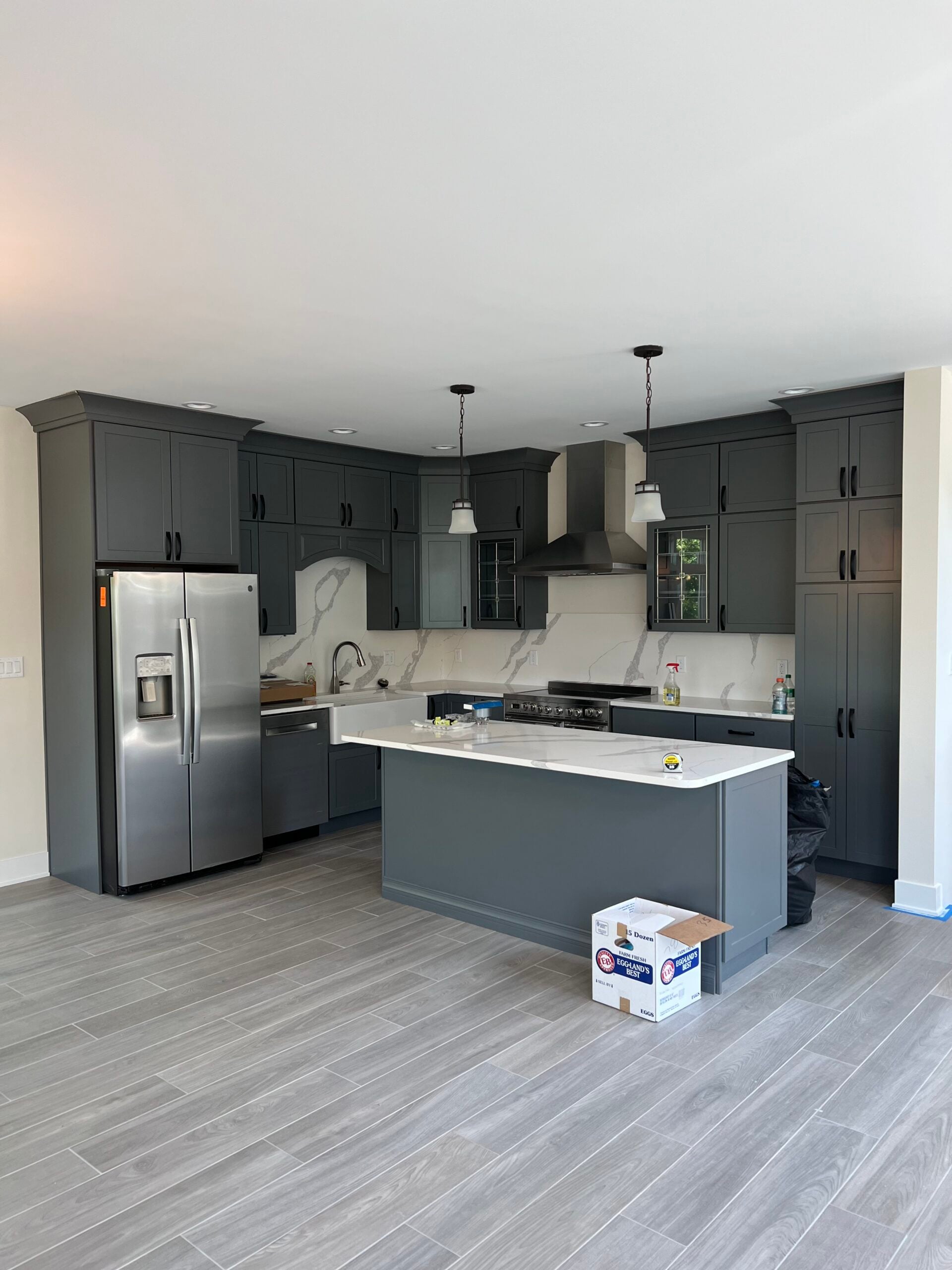 Completed kitchen remodel featuring dark gray cabinetry, white island countertop, stainless steel appliances, and pendant lighting.