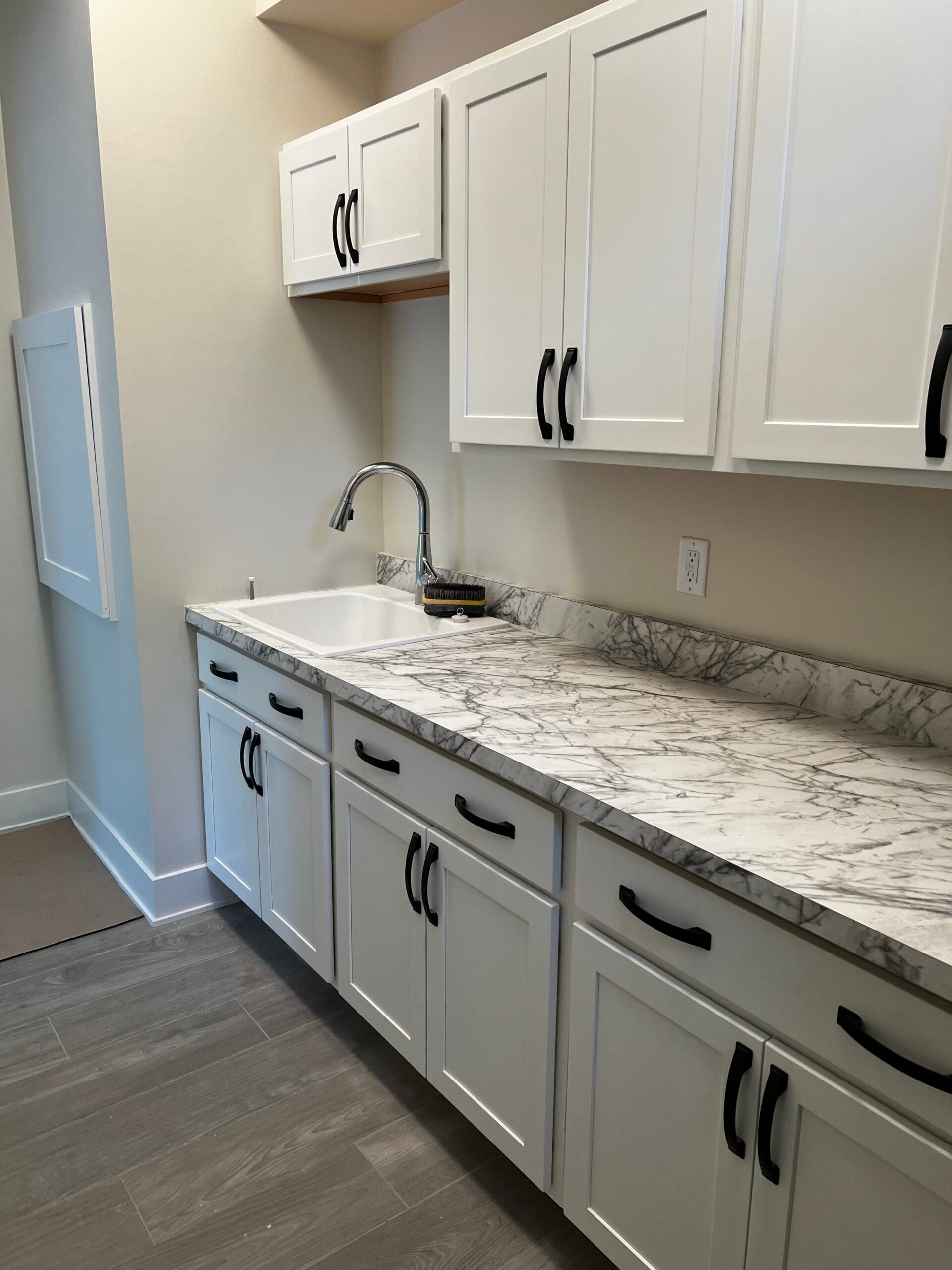 Kitchen remodel with white shaker cabinets, marble-look countertop, utility sink, and black hardware.
