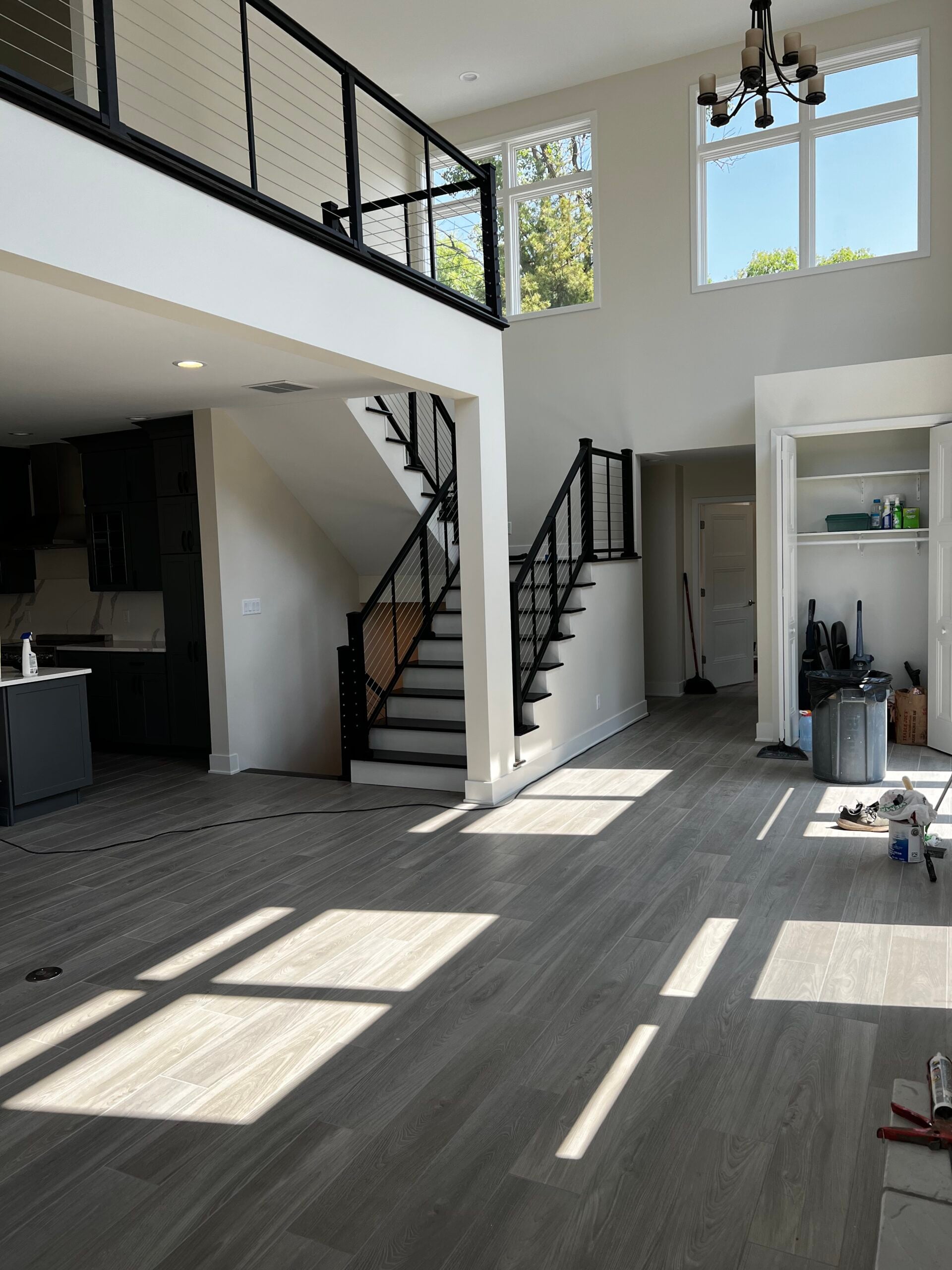 Spacious two-story interior with black cable stair railings, large windows, gray flooring, and abundant natural light.