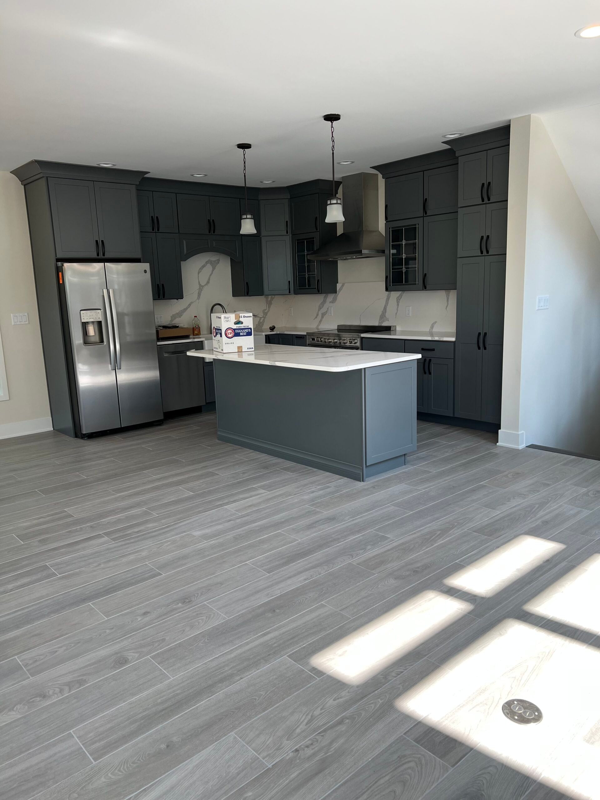 Modern kitchen remodel with dark gray cabinets, stainless steel appliances, marble-look backsplash, and a large island.