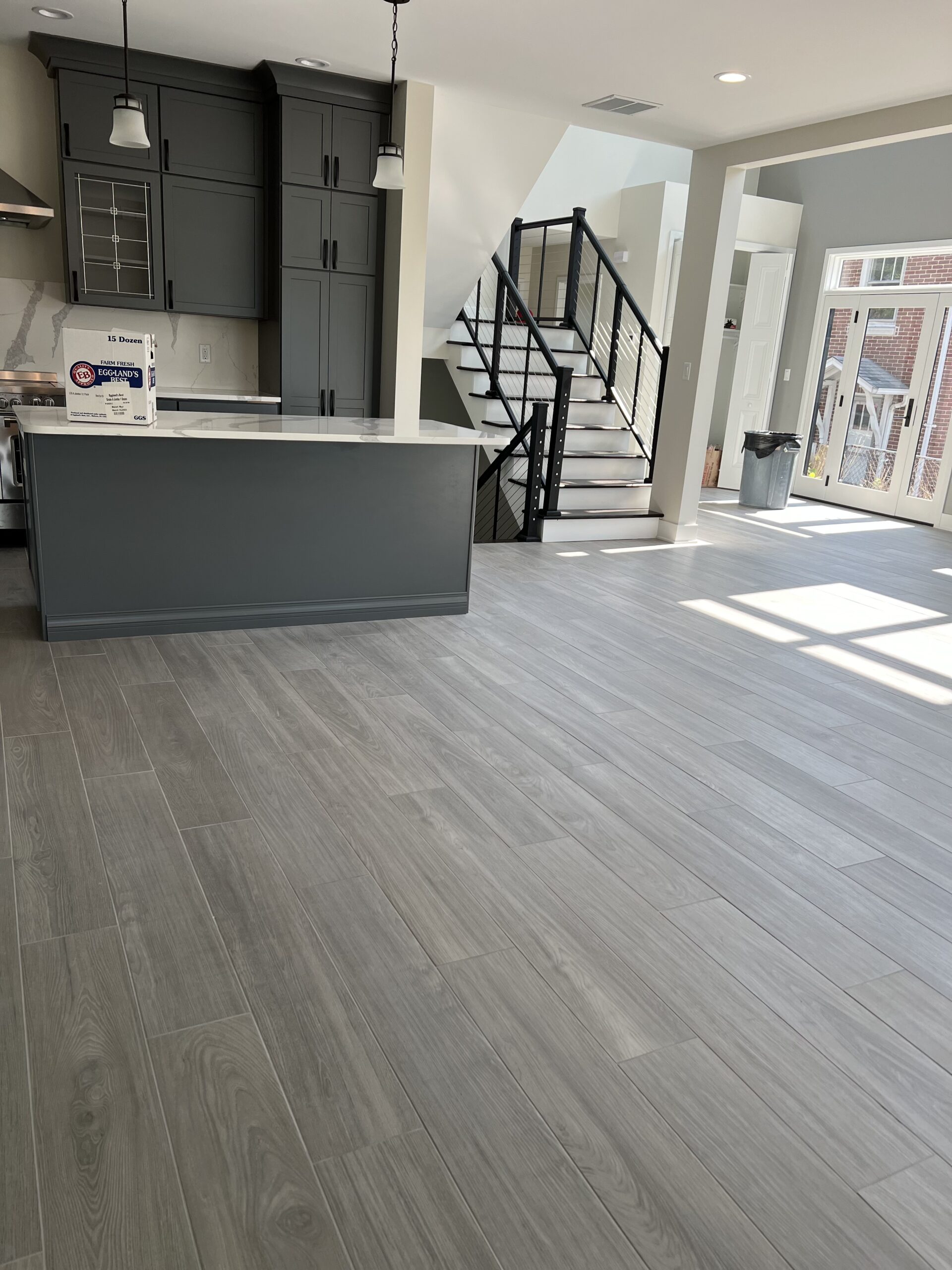 Open-concept kitchen and living space with dark gray cabinetry, white countertops, black stair railings, and gray flooring.