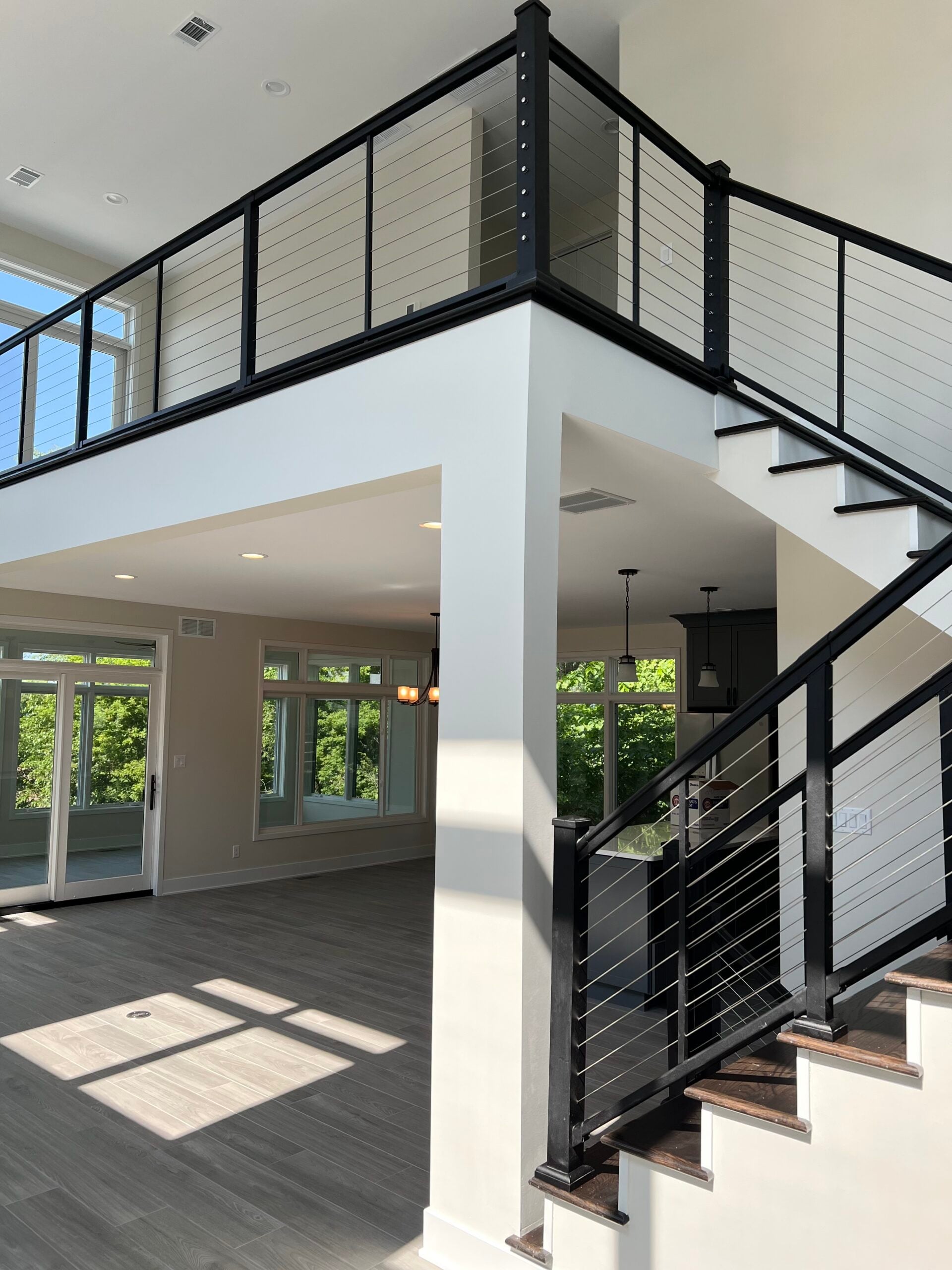 Modern home interior with black cable stair railings, dark wood stair treads, and an open-concept living area.
