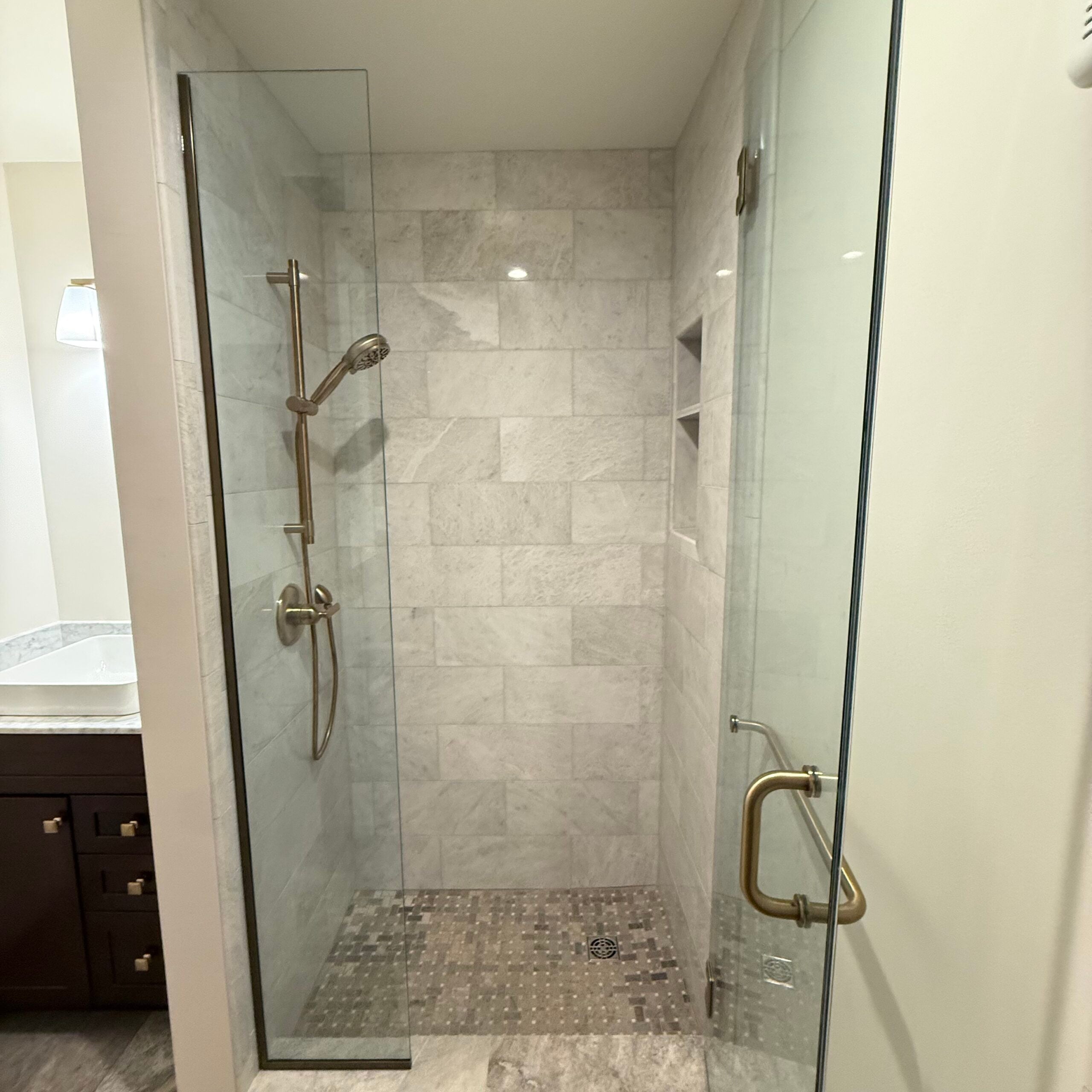 Bathroom remodeling detail showing a spacious tiled walk-in shower with glass door and brushed metal fixtures.
