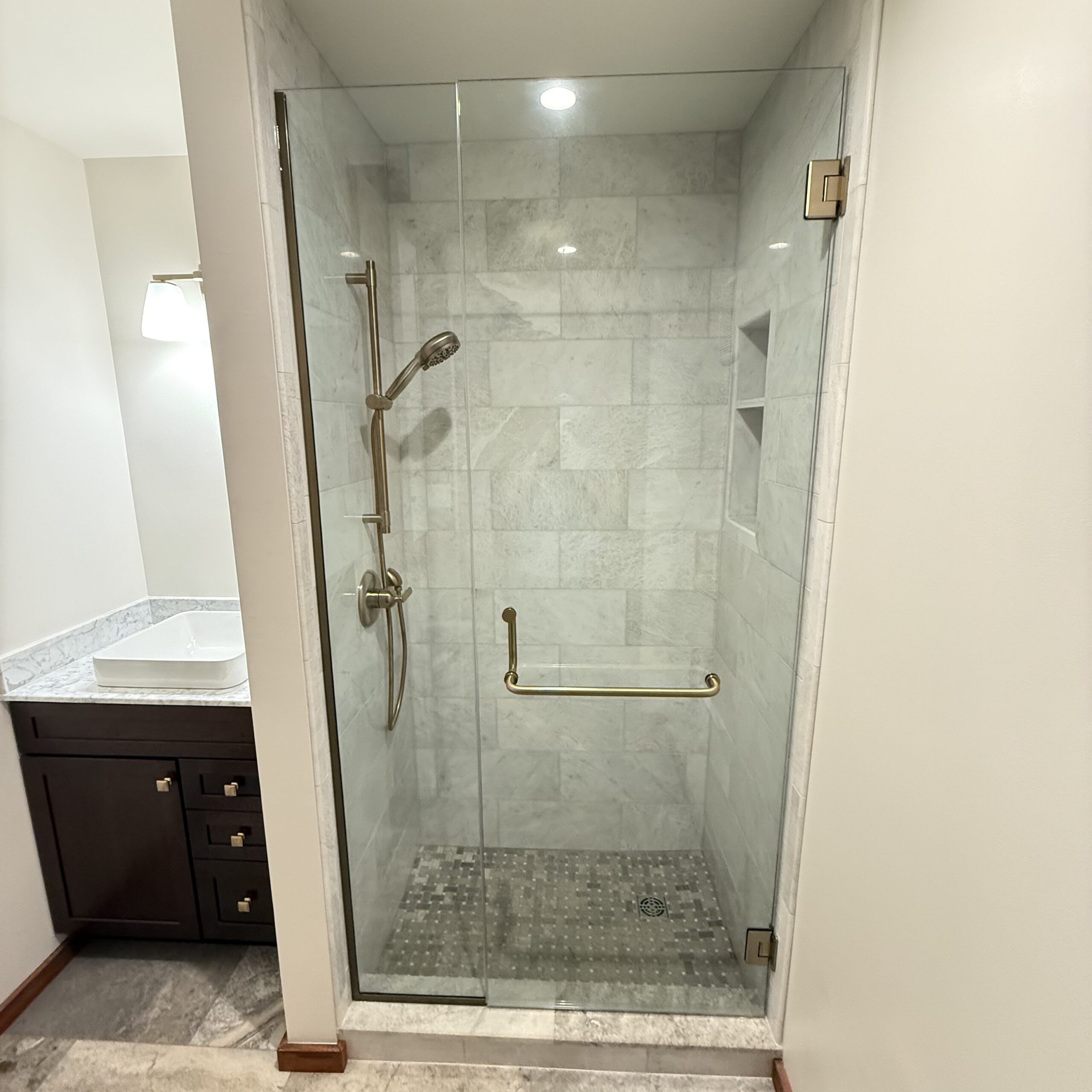 Custom walk-in shower with marble-look wall tile, mosaic shower floor, built-in shelving, and frameless glass enclosure.