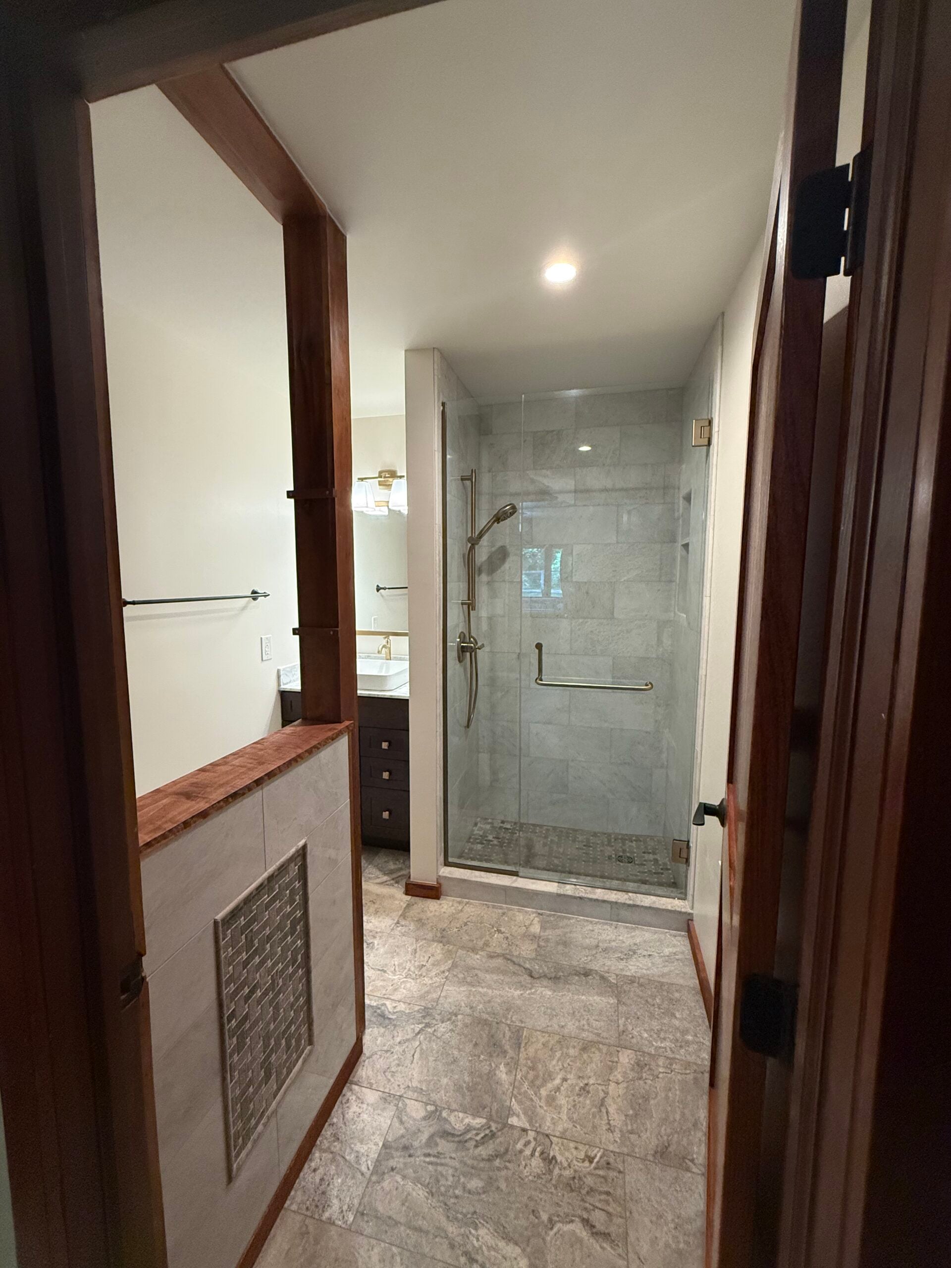 Finished bathroom remodel with marble-look flooring, custom tiled partition, dark wood vanity, and glass walk-in shower.