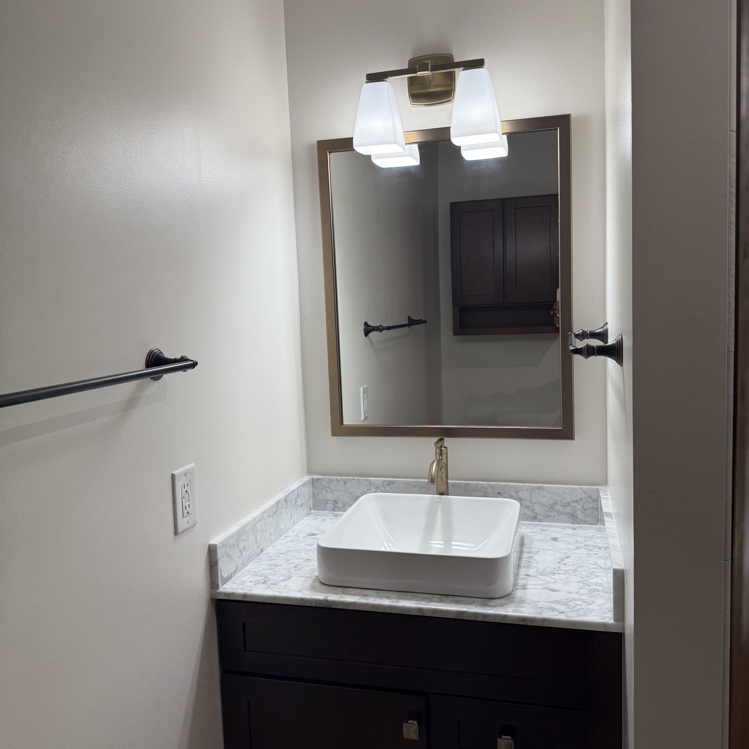 Updated bathroom vanity with dark wood cabinetry, marble-look countertop, vessel sink, framed mirror, and modern lighting.